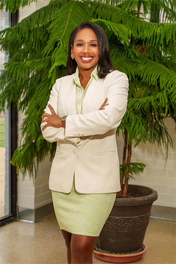 Woman in business attire in front of indoor plant smiling at camera